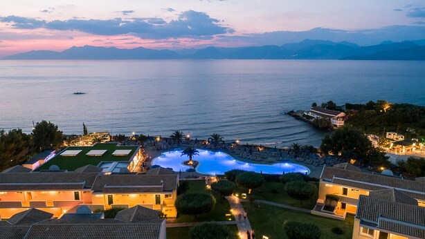 A resort with a swimming pool, villas, and a view of the sea at dusk.