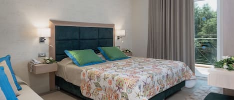 Et moderne hotelværelse med en stor seng, et sengebord med telefon og blomster, en stol og udsigt til grønne områder gennem vinduet.