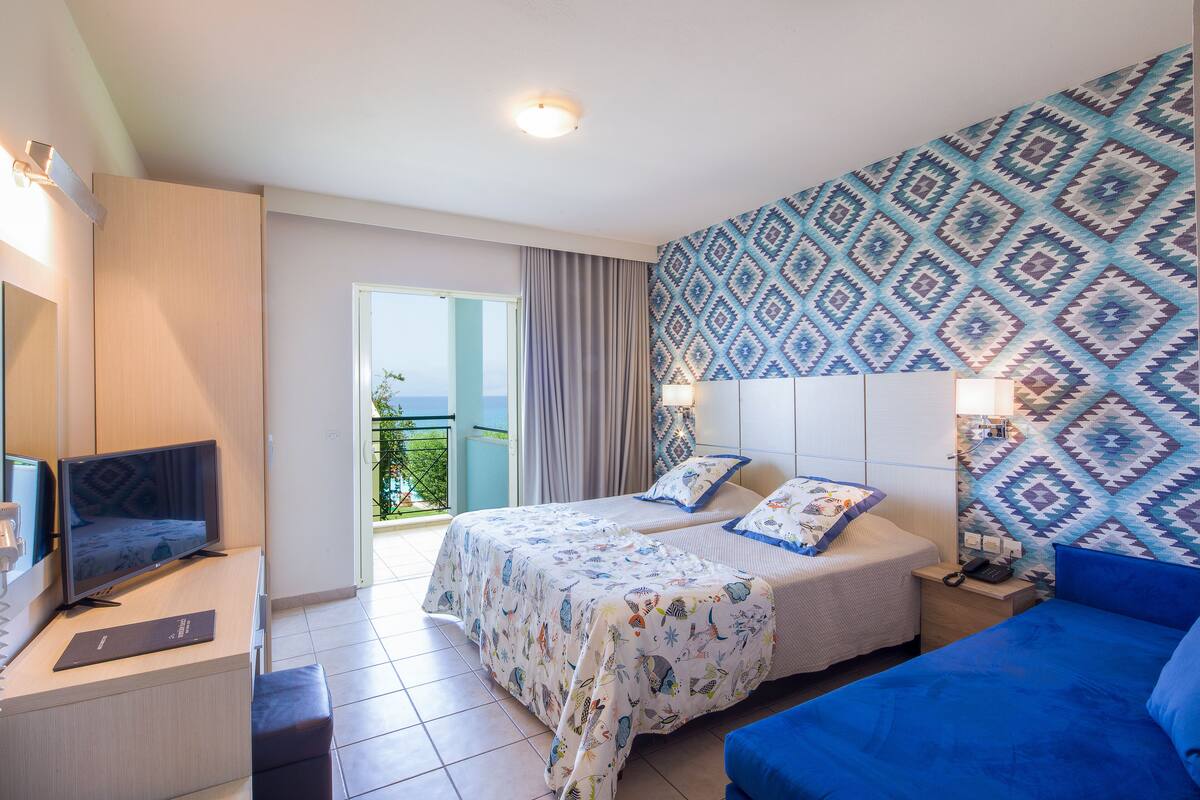 A hotel room with two beds, a TV, a desk, and a balcony with a view.