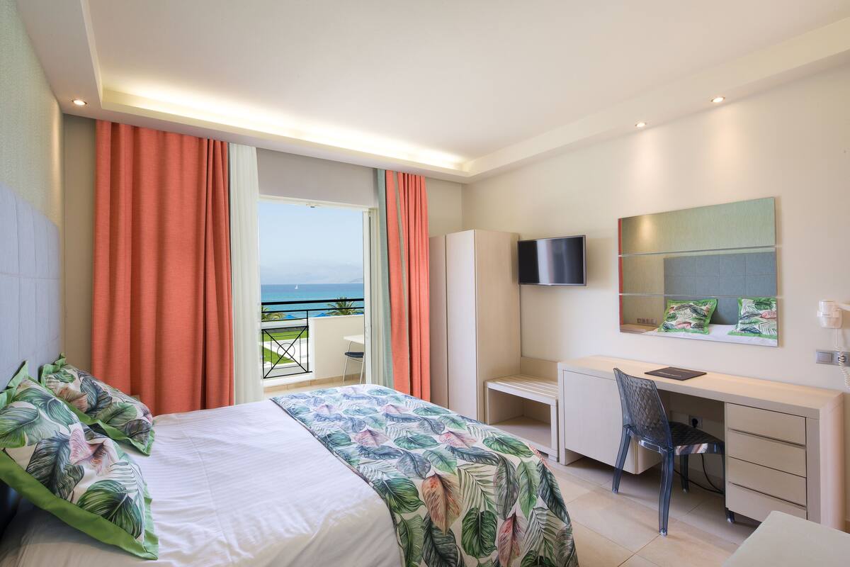 A hotel room with a bed, desk, chair, and a view of the ocean.