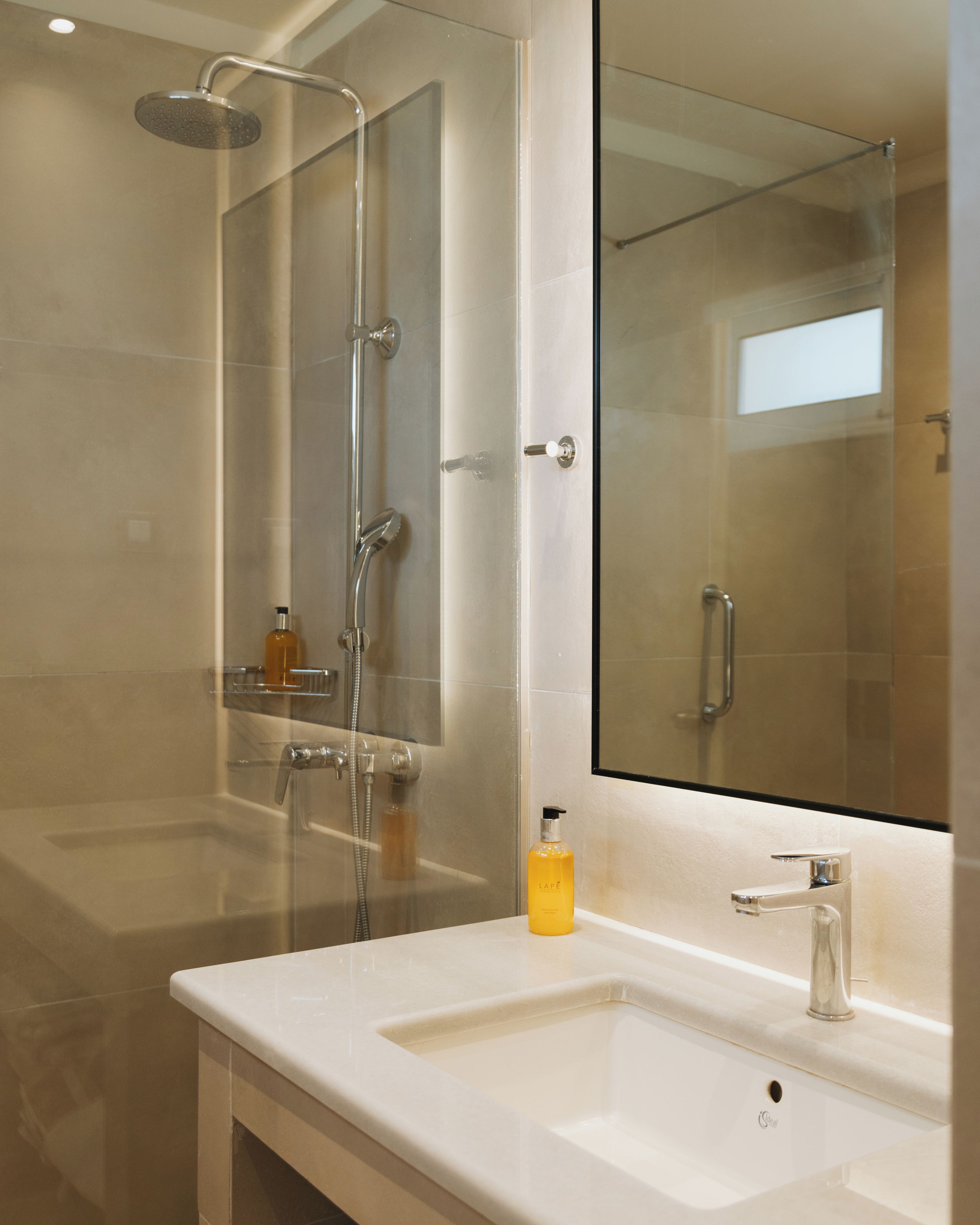A modern bathroom with a glass shower enclosure, a white sink, and a large mirror.