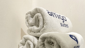 A stack of white towels with "Genting Suites" branding, a bar of soap, and two glasses of green liquid on a table.