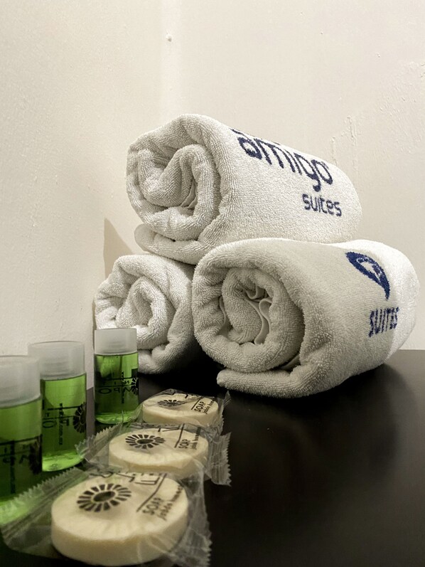A stack of white towels with "Genting Suites" branding, a bar of soap, and two glasses of green liquid on a table.