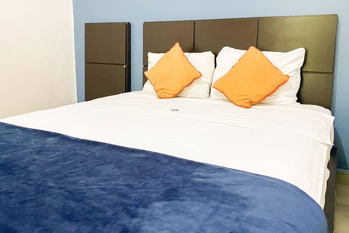Una cama con un edredón azul, almohadas blancas y dos almohadas naranjas.