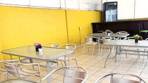 An outdoor dining area with metal tables and chairs, surrounded by yellow walls and a tiled floor.