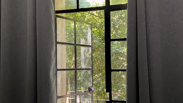 A room with a large window, curtains, and a view of greenery outside.