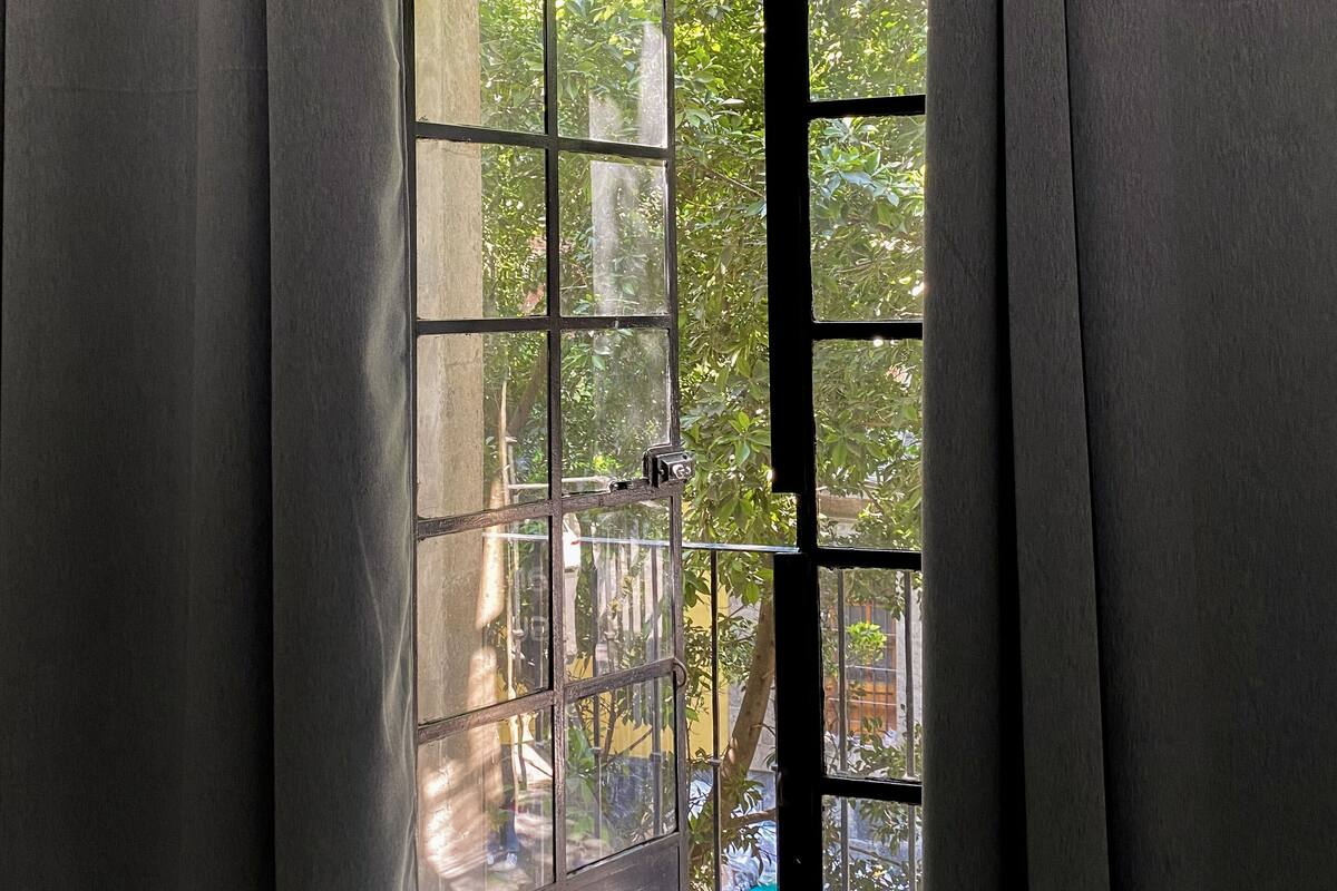Una habitación con un gran ventanal, cortinas y vistas al verdor exterior.