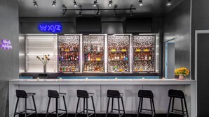A bar area with a neon sign reading "WXYZ," bar stools, and shelves stocked with bottles. - Aloft by Marriott New York Brooklyn (Brooklyn)