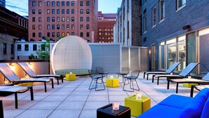 An outdoor seating area with lounge chairs and tables, a spherical structure, and a cityscape in the background. - Aloft by Marriott New York Brooklyn (Brooklyn)