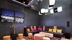 A modern lounge area with a sectional sofa, round ottomans, and a patterned rug.
