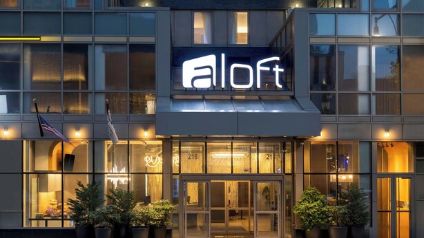 A modern hotel with a prominent 'Alloft' sign, large windows, and potted plants at the entrance. - Aloft by Marriott New York Brooklyn (Brooklyn)