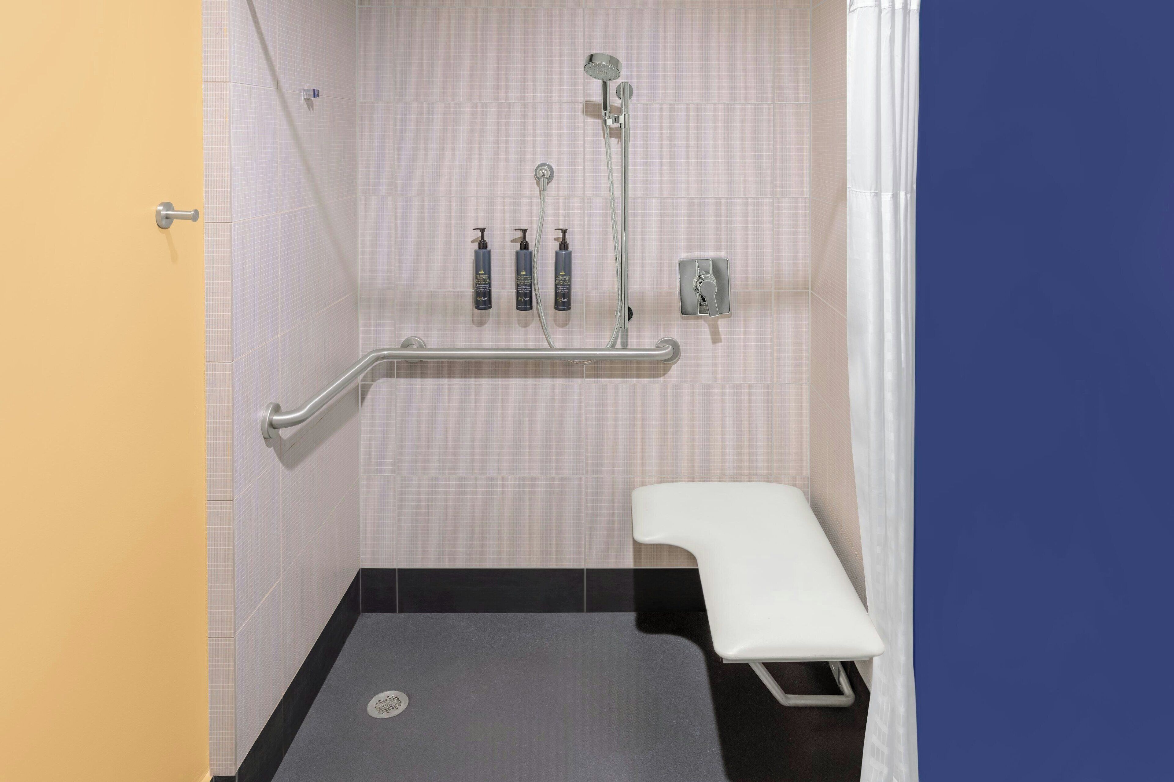 Un baño con ducha, un banco y dispensadores de gel antibacterial.