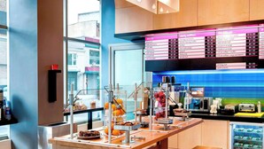 A modern cafe with a wooden table and benches, a menu board, and a view of the street outside. - Aloft by Marriott New York Brooklyn (Brooklyn)