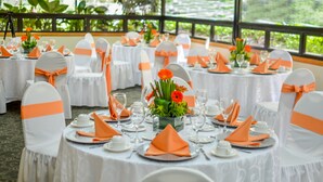 Une salle de banquet avec des tables rondes dressées pour un événement formel, agrémentée de nappes blanches et de rubans orange sur les chaises.