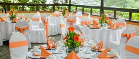 A banquet hall with round tables set for a formal event, featuring white tablecloths and orange sashes on chairs.