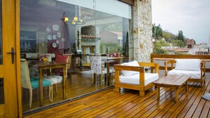A wooden deck with outdoor furniture, a glass wall, and a view of a building with a tiled roof. - Kkala Boutique Hotel (Salta)