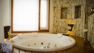 Ein Spa-Raum mit Whirlpool, Holzboden, Steinwand und einem Fenster mit Jalousien.