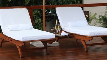 Two wooden lounge chairs with white cushions and a small table with a bottle and glasses.