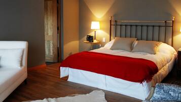 Una habitación de hotel con una cama, un sillón blanco, una mesita de noche con una lámpara y otro sillón estampado.