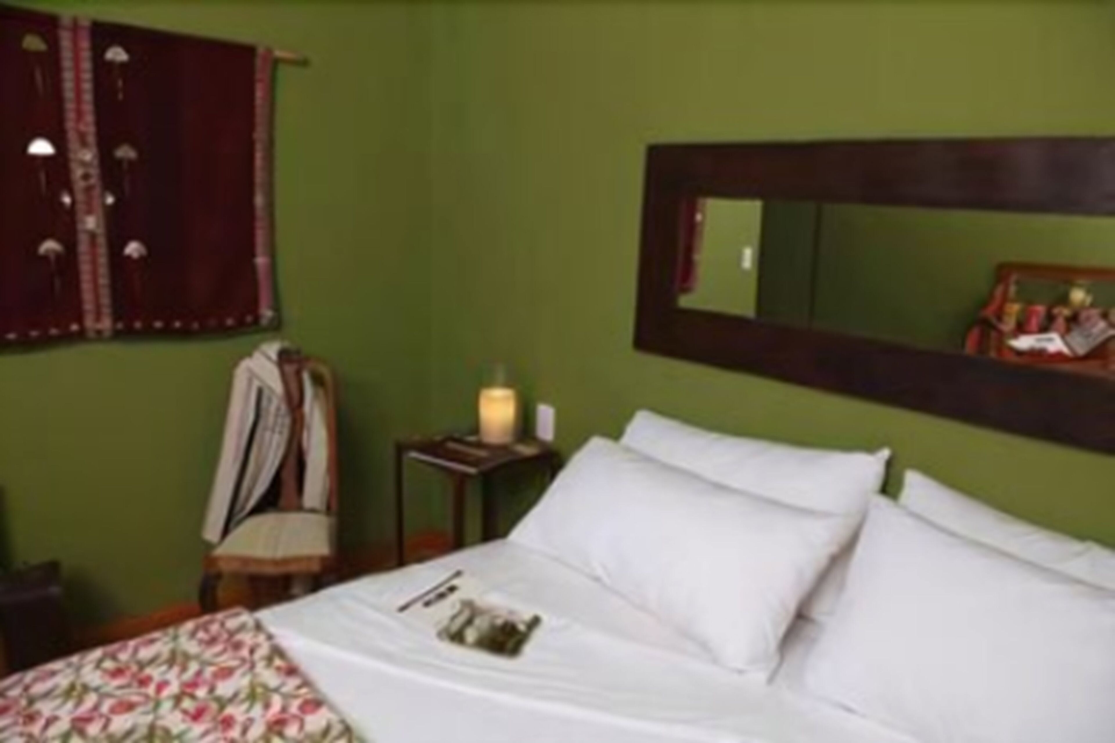 A room with a bed, a mirror, a nightstand with a candle, and a chair.