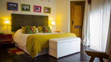 A bedroom with a bed, bedside lamps, a wooden floor, a bench, and a door.