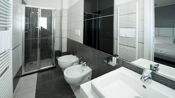 Un bagno moderno con doccia vetro, bidet, lavandino capiente e specchio.