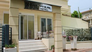 Entrada de un hotel con un letrero que dice "Atmosphere Hotel", una puerta de vidrio y un pequeño espacio al aire libre con plantas en macetas.