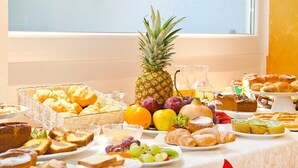 Un bufé de desayuno con diversos pasteles, frutas y una piña como centro de mesa.
