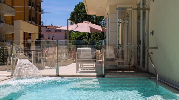 Piscina con fuente de agua, barandillas de vidrio y mobiliario exterior.