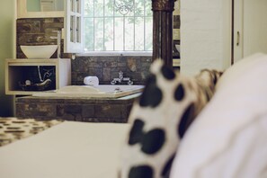 Une salle de bain avec un mur en pierre, un lavabo blanc et une fenêtre avec des barreaux.
