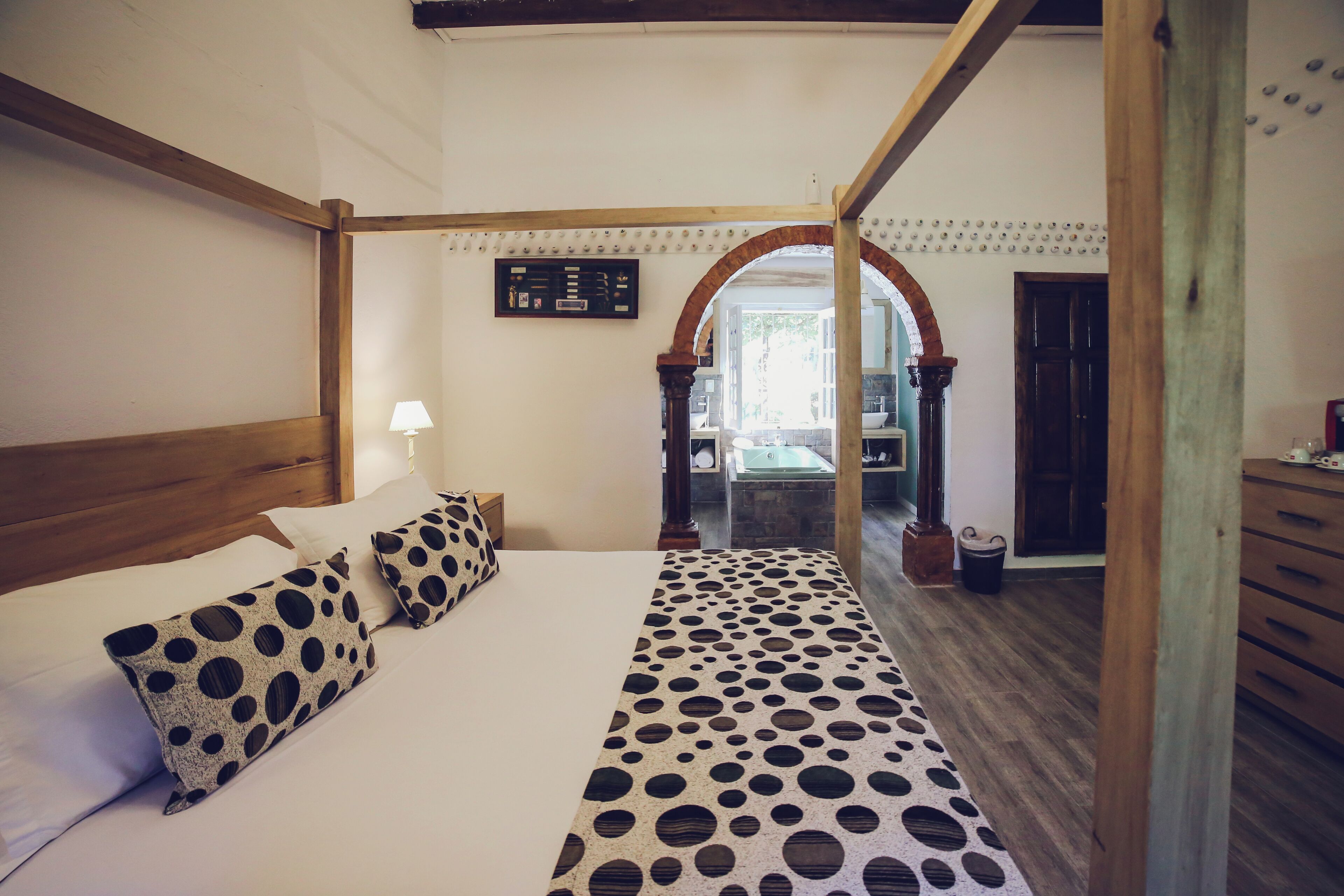 Quarto com cama de dossel, cabeceira de madeira e colcha de bolinhas.