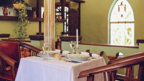 A dining table set with plates, glasses, and a candle, surrounded by wooden chairs in a room with a stained glass window. - Villa Toscana Boutique Hotel - Adults only (Punta Ballena)