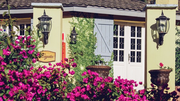 Un bâtiment avec une enseigne indiquant « Café », des plantes en pot et une fenêtre avec des volets.