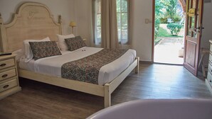 A bedroom with a bed, bedside tables, a lamp, and a view of the garden through an open door. - Villa Toscana Boutique Hotel - Adults only (Punta Ballena)