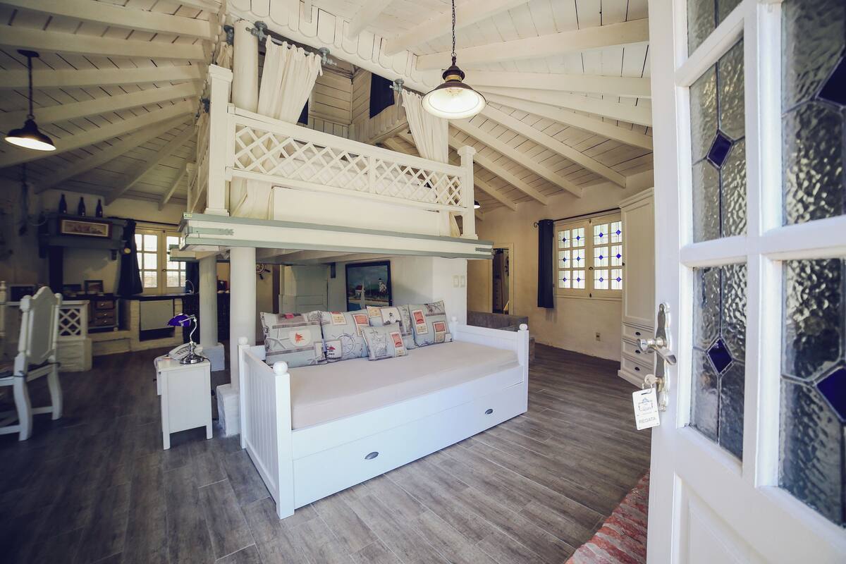 Una habitación amplia con cama tipo altillo, una mesita y una silla.