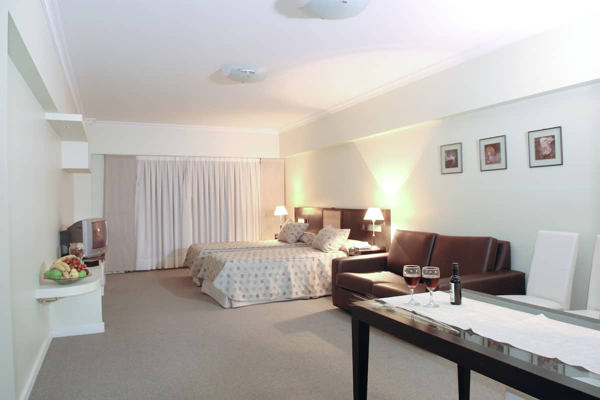 A hotel room with a bed, a sofa, a table with glasses and a bottle, and a TV.
