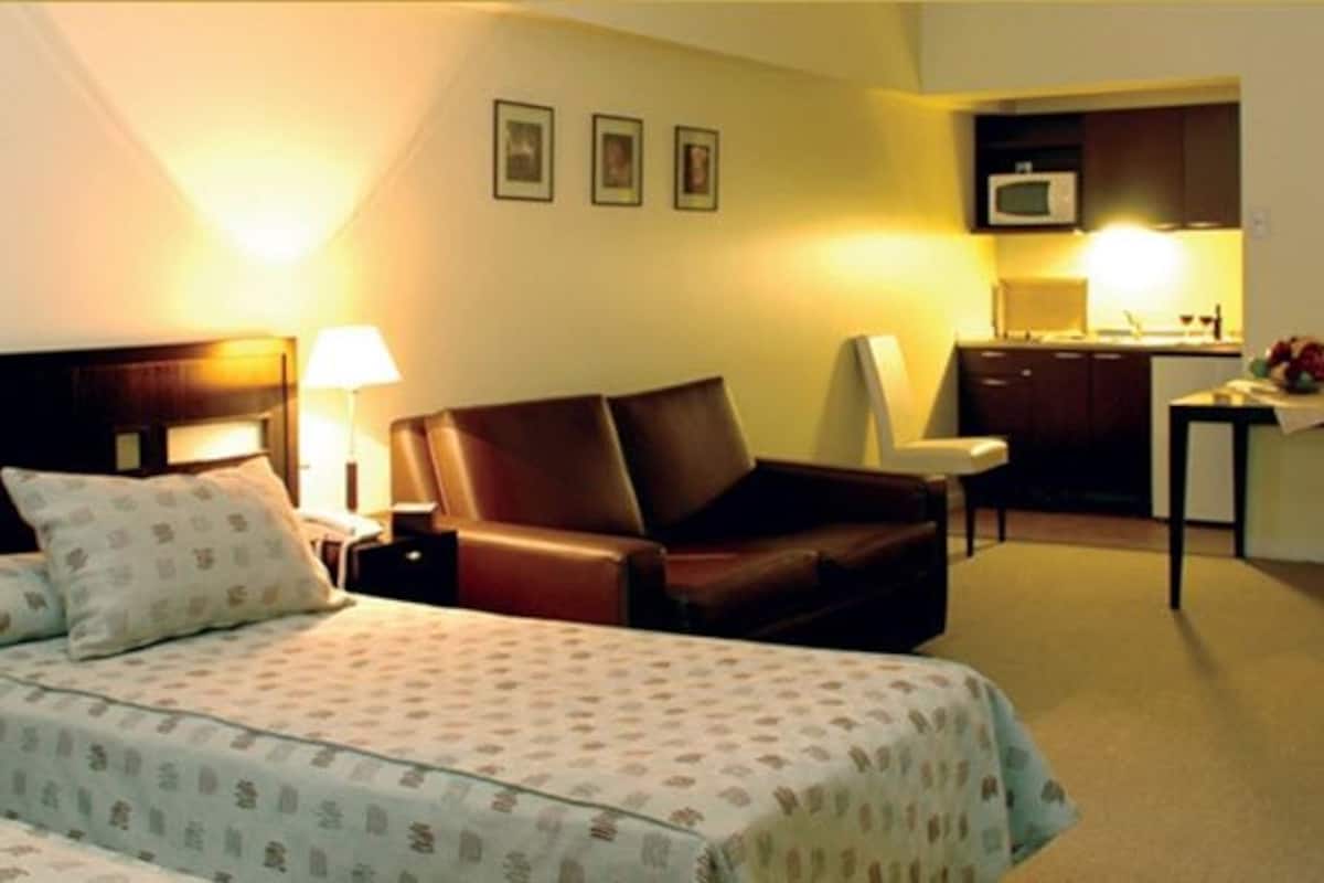 A hotel room with two beds, a desk, a chair, a microwave, and a small kitchen area.