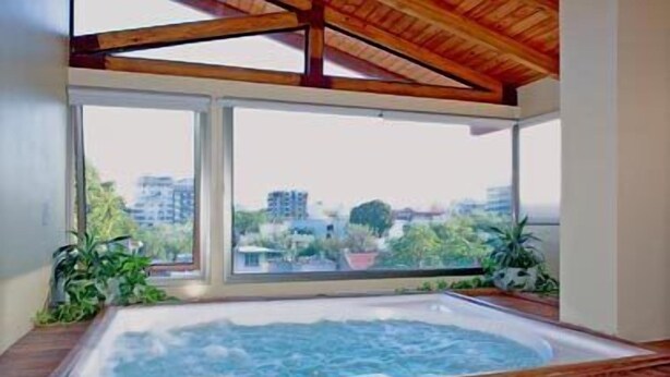 Un jacuzzi con vista a la ciudad, vigas de madera en el techo y plantas en macetas.