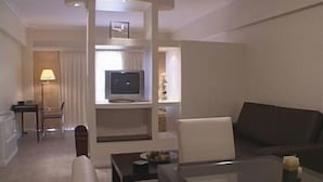 Una habitación de hotel con un sofá de color oscuro, una mesita con una vela, un televisor sobre un mueble y una silla.