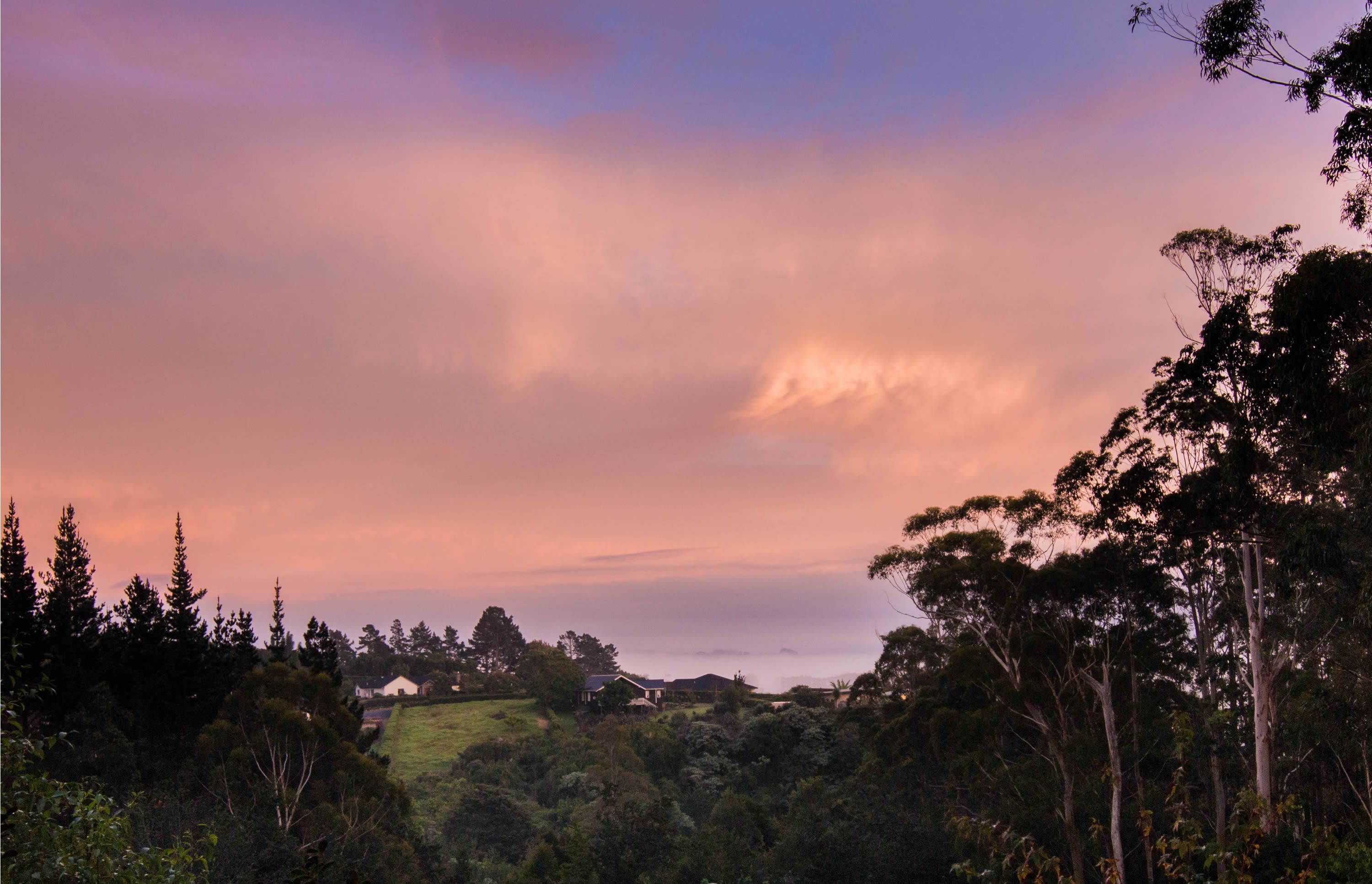 A landscape with a house surrounded by trees and hills.