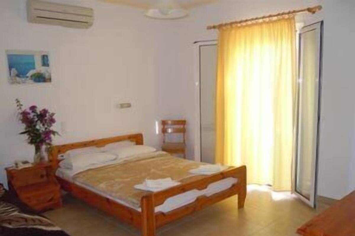 Un dormitorio con una cama de madera, una mesita de noche, una silla, una ventana con cortinas y un aire acondicionado instalado en la pared.