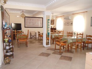 A dining area with wooden chairs and tables, a television, and a decorative wall piece. - Pension Atlas (Santorini)