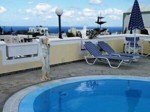 A swimming pool with lounge chairs and a view of the sea. - Pension Atlas (Santorini)