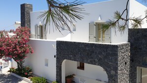 Um edifício branco com paredes de pedra e janelas com persianas, uma varanda e um vaso de planta.