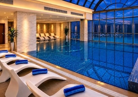 A modern indoor swimming pool with lounge chairs and a glass ceiling.