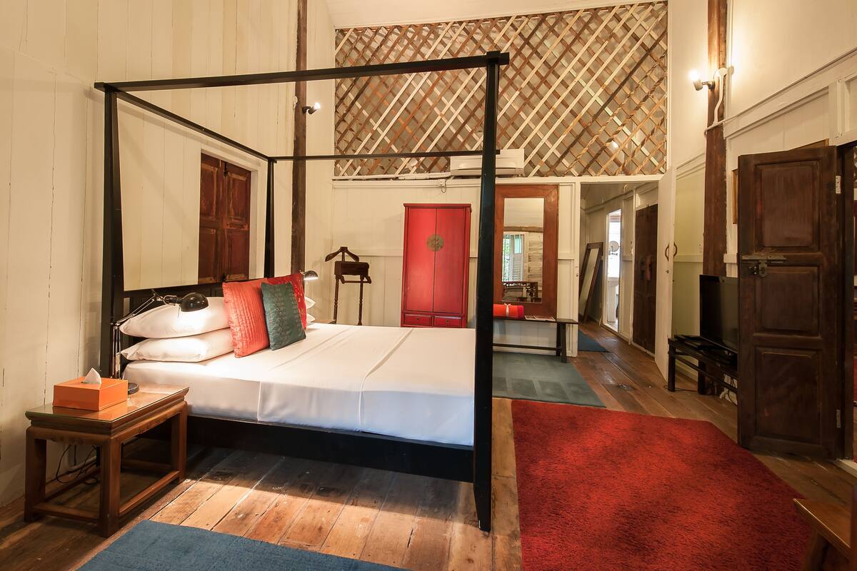 A four-poster bed with a wooden frame, a red door in the background, and a red carpet leading to a hallway.