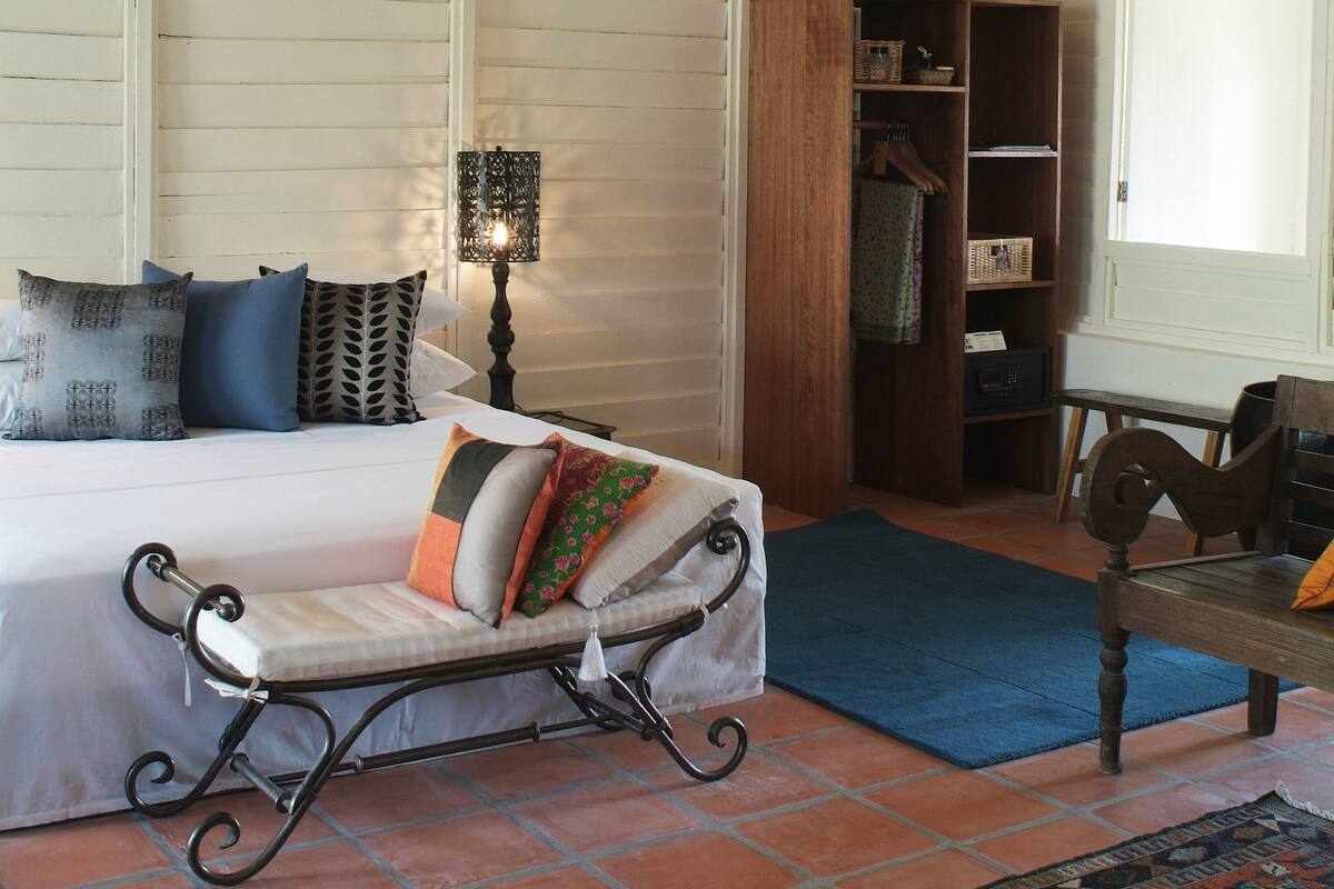 A bedroom with a bed, a wooden wardrobe, a desk, and a patterned rug.