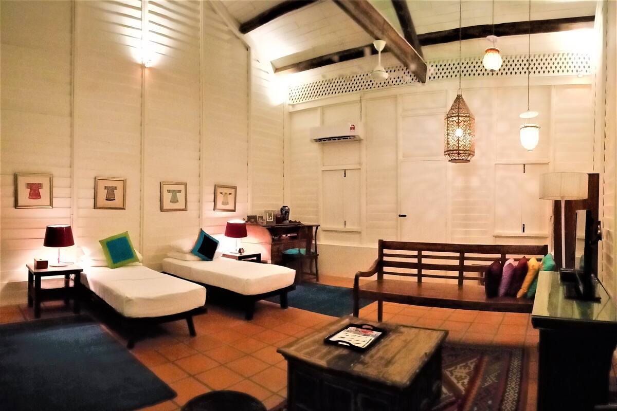 A cozy room with two single beds, a wooden bench, a small table, and a hanging light fixture.