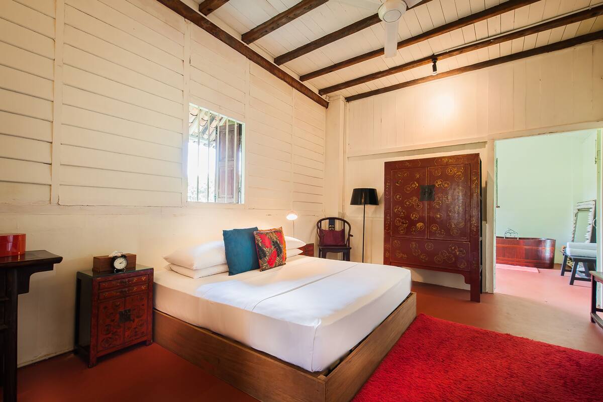A bedroom with a wooden bed, a red rug, a nightstand with a clock, and a wardrobe.