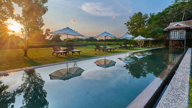 A serene pool area with lounge chairs and umbrellas, surrounded by lush greenery and a clear sky. - Temple Tree at Bon Ton (Langkawi)